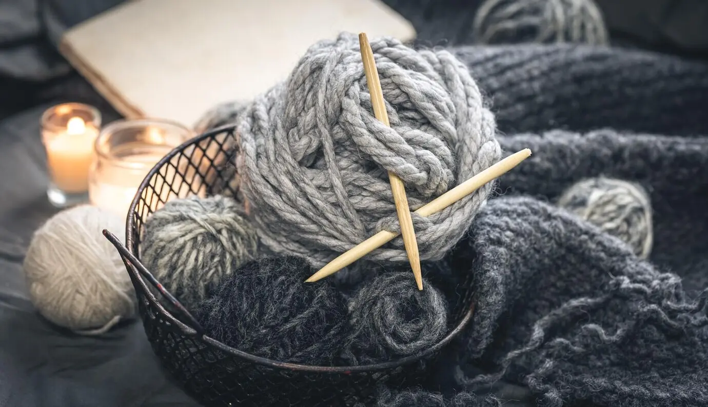 Nahaufnahme grauer Strickgarnfäden mit hölzernen Stricknadeln.